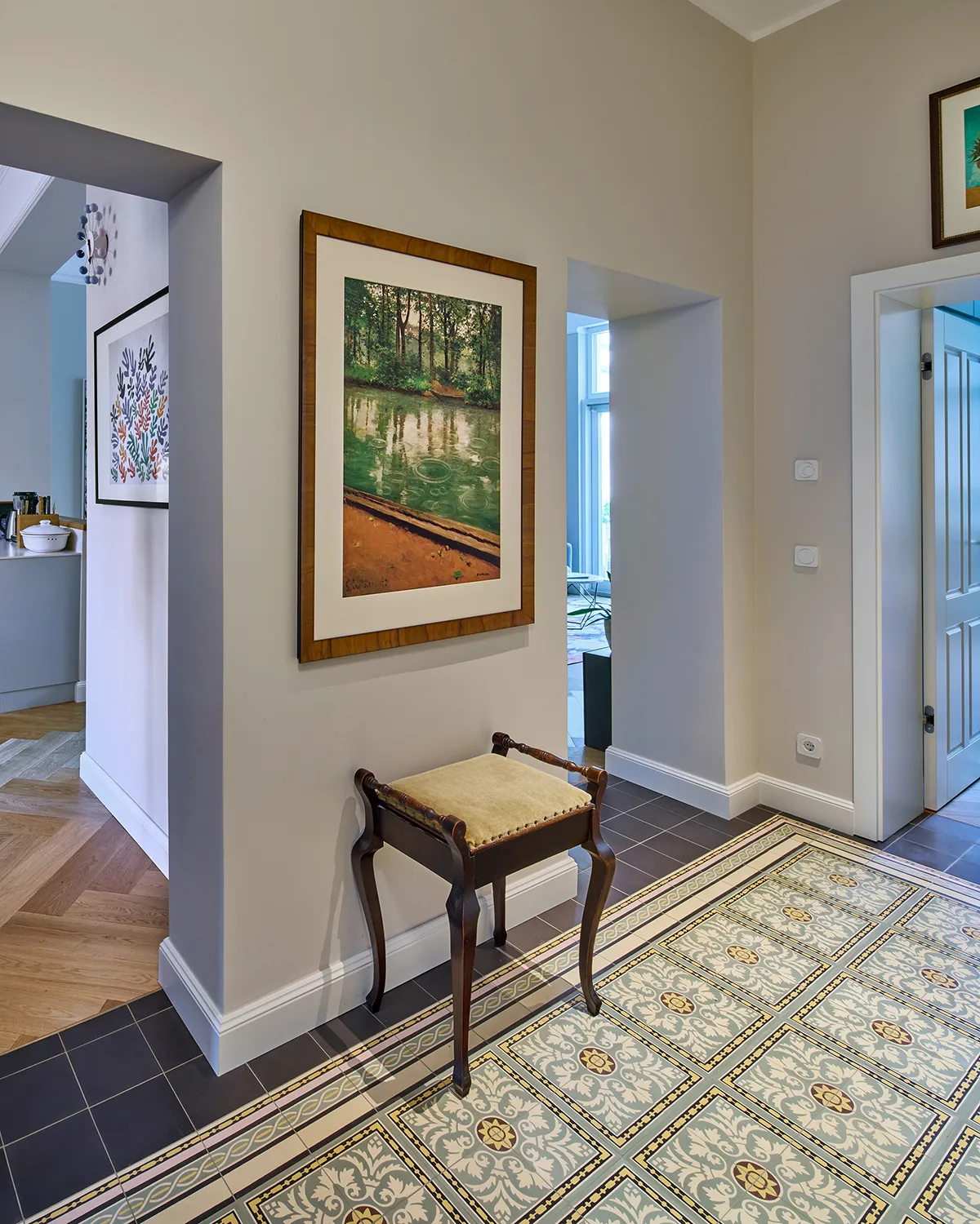 Eingangsdiele einer modernisierten Maisonettewohnung mit originalgetreuen Jugendstilfliesen, klarer Wandgestaltung und Durchgang zur offenen Küche.